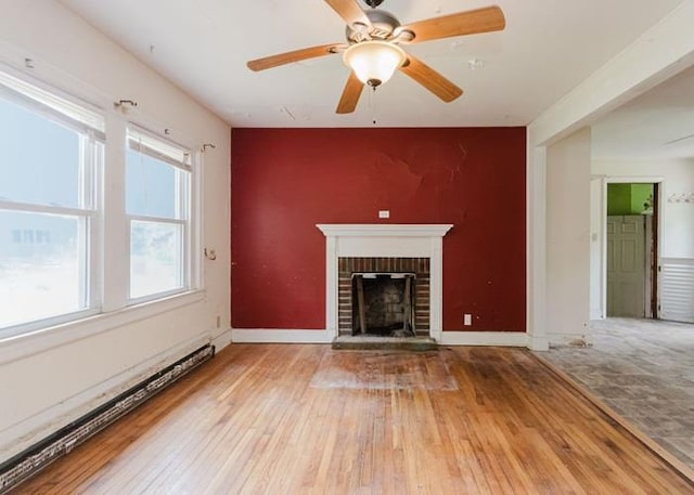 8 Gary Dr, Hyde Park, NY 12538 - unfurnished living room featuring a baseboard radiator, an accent wall, hardwood / wood-style floors, a brick fireplace, and a ceiling fan