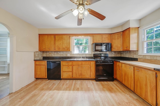 126 Carman St, Patchogue, NY 11772 - kitchen with black appliances, brown cabinetry, light wood-style flooring, arched walkways, and plenty of natural light