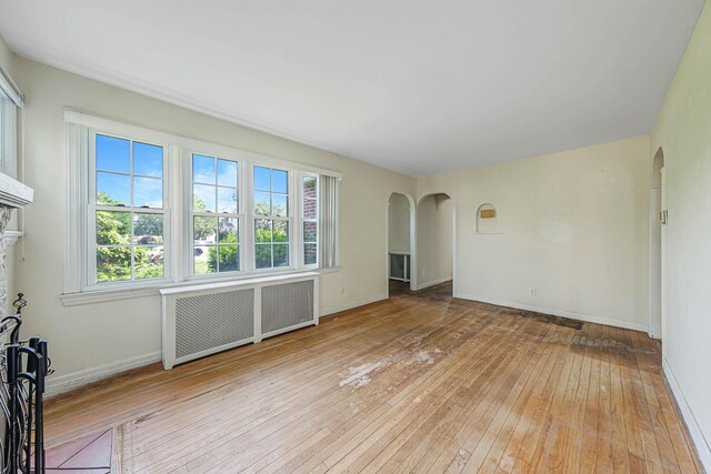 126 Carman St, Patchogue, NY 11772 - unfurnished room with radiator heating unit, arched walkways, light wood finished floors, and healthy amount of natural light