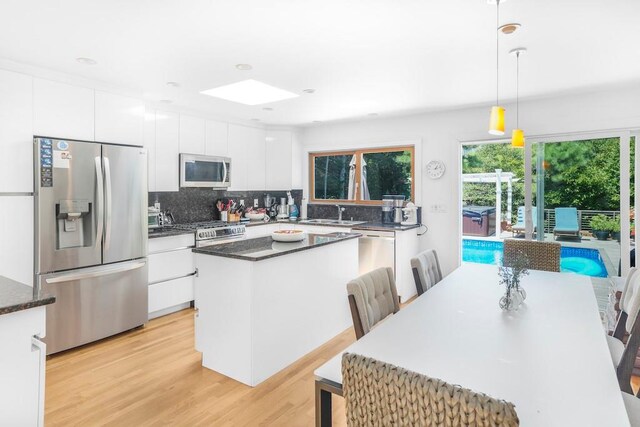 305 Fire Island Blvd, Fire Island Pines, NY 11782 - kitchen featuring appliances with stainless steel finishes, a center island, light wood-style floors, tasteful backsplash, and white cabinets