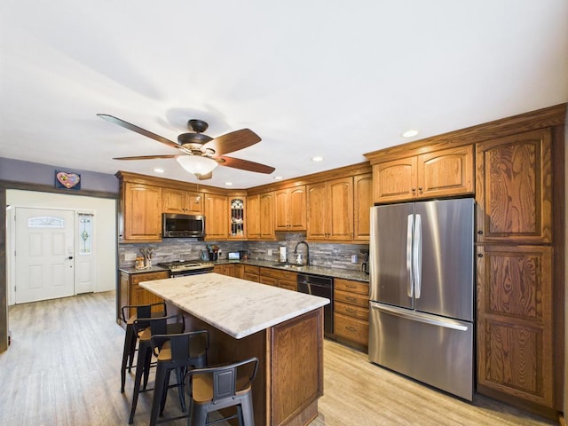 12 Turin St, East Patchogue, NY 11772 - kitchen with stainless steel appliances, brown cabinetry, a ceiling fan, a kitchen breakfast bar, and backsplash