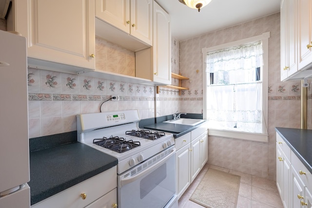 251 Seaman Ave Unit 6A, New York Manhattan, NY 10034 - kitchen featuring white gas range, freestanding refrigerator, dark countertops, light tile patterned floors, and tile walls