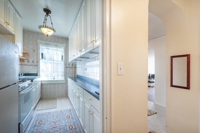 251 Seaman Ave Unit 6A, New York Manhattan, NY 10034 - kitchen featuring light tile patterned floors, arched walkways, white cabinetry, and wallpapered walls