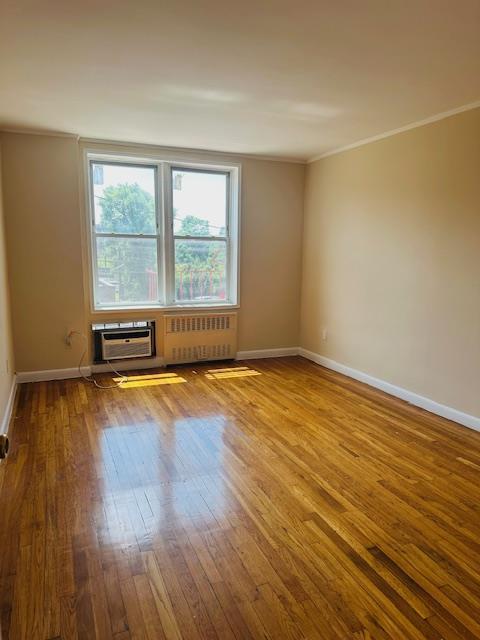 86-05 60th Rd Unit 2E, Elmhurst, NY 11373 - empty room featuring radiator, hardwood / wood-style floors, crown molding, and an AC wall unit