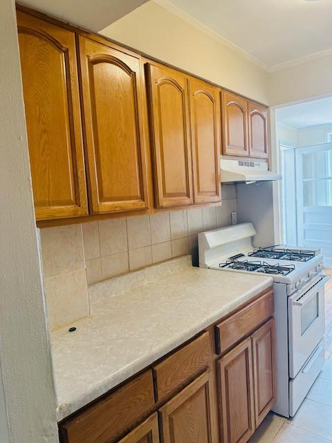 86-05 60th Rd Unit 2E, Elmhurst, NY 11373 - kitchen with white gas range, under cabinet range hood, light countertops, decorative backsplash, and crown molding