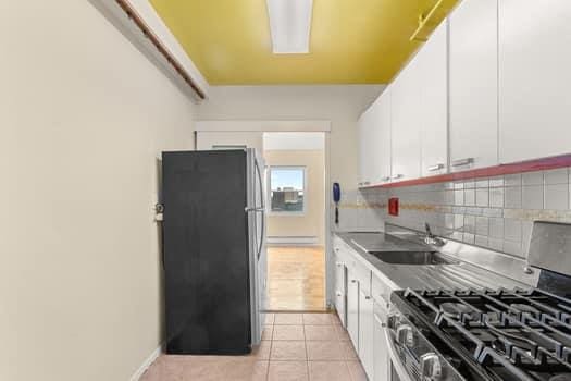 4 Fordham Hill Oval Unit 12B, Bronx, NY 10468 - kitchen with stainless steel appliances, decorative backsplash, white cabinets, a baseboard heating unit, and light tile patterned floors