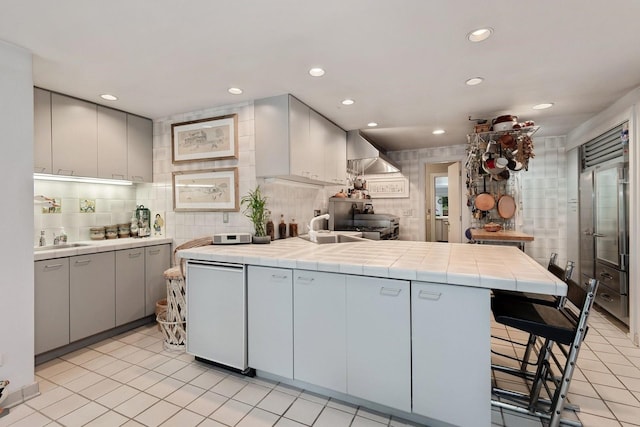 56 Tuthill Point Rd, East Moriches, NY 11940 - kitchen featuring a peninsula, tile countertops, wall chimney exhaust hood, backsplash, and light tile patterned flooring