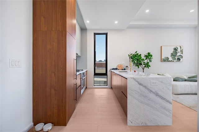 3116 21st St Unit Ph2F, Astoria, NY 11106 - kitchen featuring modern cabinets, a peninsula, brown cabinets, recessed lighting, and light stone counters