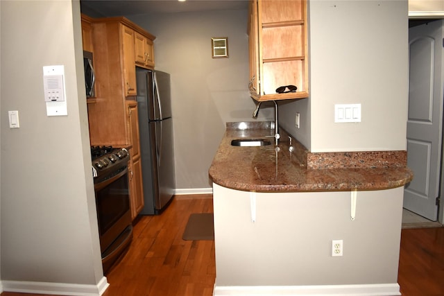 596 Broadway Unit 10B, Lynbrook, NY 11563 - kitchen featuring stainless steel appliances, wood finished floors, a peninsula, a kitchen bar, and dark stone countertops
