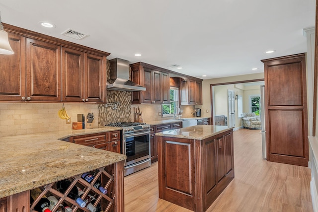 246 Cadman Ave, Babylon, NY 11702 - kitchen with stainless steel range with gas stovetop, wall chimney exhaust hood, light stone counters, light wood-style flooring, and a kitchen island
