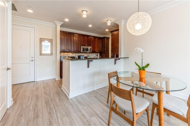 1 Christie Pl Unit 205E, Scarsdale, NY 10583 - kitchen featuring stainless steel microwave, dark countertops, crown molding, a breakfast bar area, and light wood-type flooring