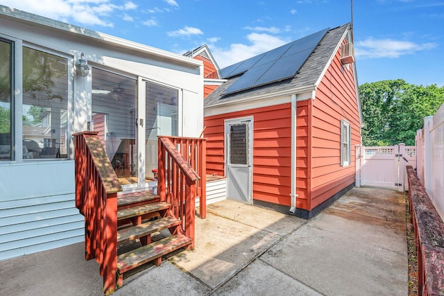694 Koelbel Ct, Baldwin, NY 11510 - rear view of house with a gate, roof mounted solar panels, roof with shingles, a sunroom, and a patio