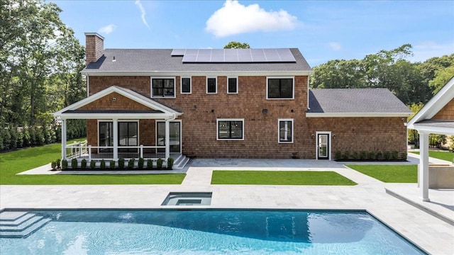 128 Sandy Hollow Rd, Southampton, NY 11968 - rear view of property featuring a patio area, a chimney, solar panels, roof with shingles, and a lawn