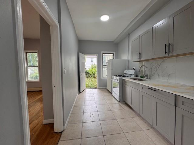 10326 171st St, Jamaica, NY 11433 - kitchen featuring white range with gas stovetop, gray cabinetry, light countertops, tasteful backsplash, and light tile patterned floors