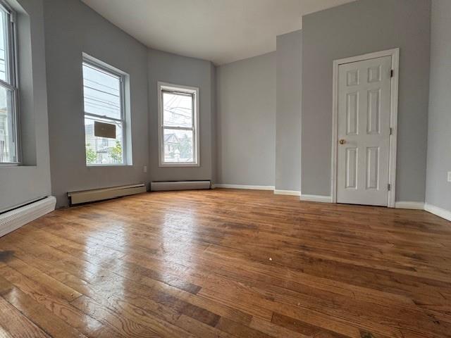 10326 171st St, Jamaica, NY 11433 - spare room featuring wood finished floors and a baseboard heating unit