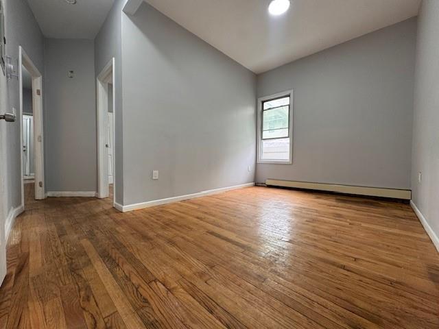 10326 171st St, Jamaica, NY 11433 - unfurnished room with baseboard heating, wood finished floors, and vaulted ceiling