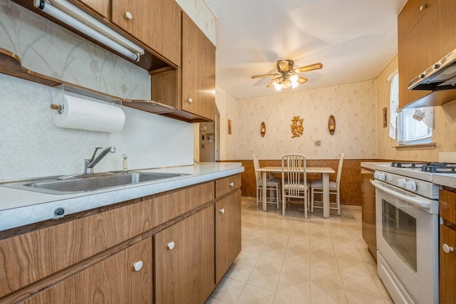 66 Gates Ave, Valley Stream, NY 11580 - kitchen featuring gas range gas stove, wallpapered walls, brown cabinetry, a ceiling fan, and a wainscoted wall