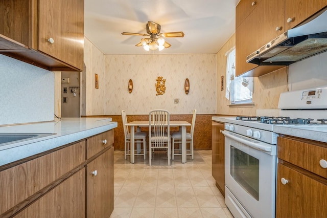 66 Gates Ave, Valley Stream, NY 11580 - kitchen with gas range gas stove, wallpapered walls, under cabinet range hood, ceiling fan, and brown cabinets