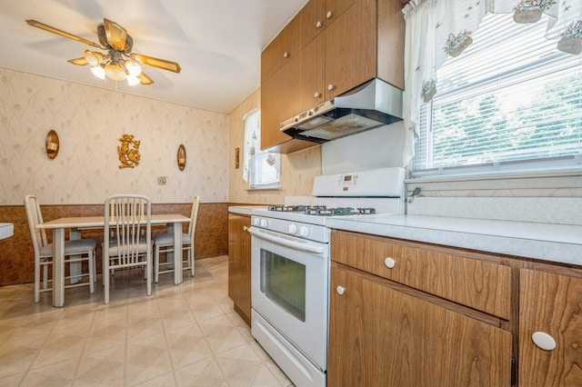 66 Gates Ave, Valley Stream, NY 11580 - kitchen with white gas stove, wallpapered walls, exhaust hood, brown cabinetry, and ceiling fan
