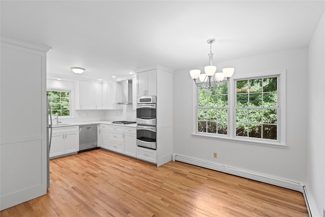 21 Kipp St, Chappaqua, NY 10514 - kitchen featuring appliances with stainless steel finishes, a baseboard radiator, wall chimney range hood, white cabinets, and light wood-style floors