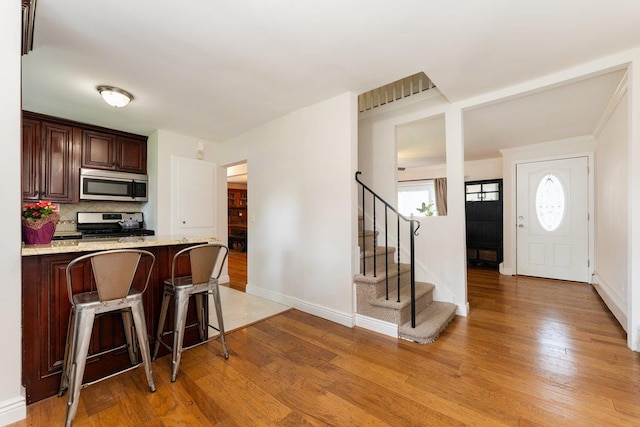 2691 Evans Rd, Oceanside, NY 11572 - kitchen with appliances with stainless steel finishes, a breakfast bar, light wood finished floors, tasteful backsplash, and dark brown cabinets
