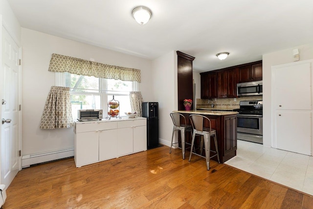 2691 Evans Rd, Oceanside, NY 11572 - kitchen with stainless steel appliances, baseboard heating, backsplash, light countertops, and a kitchen bar