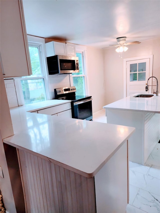 13SLake Drive, Patterson, NY 12563 - kitchen featuring appliances with stainless steel finishes, a peninsula, light countertops, white cabinets, and light marble finish flooring