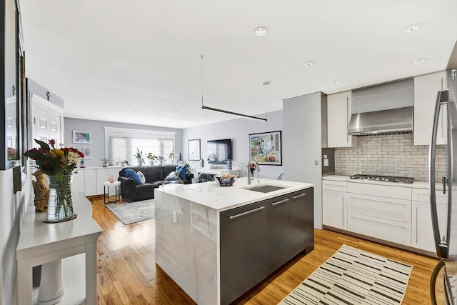 2723 Tilden Ave, Brooklyn, NY 11226 - kitchen featuring a kitchen island with sink, decorative backsplash, wall chimney range hood, light wood-style floors, and appliances with stainless steel finishes