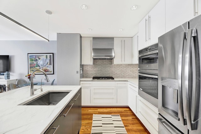 2723 Tilden Ave, Brooklyn, NY 11226 - kitchen featuring appliances with stainless steel finishes, wall chimney range hood, light wood-style flooring, backsplash, and light stone countertops