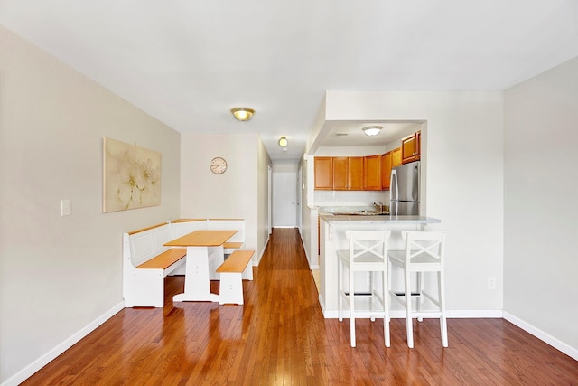 2723 Tilden Ave, Brooklyn, NY 11226 - kitchen featuring freestanding refrigerator, wood finished floors, brown cabinets, a breakfast bar area, and light countertops