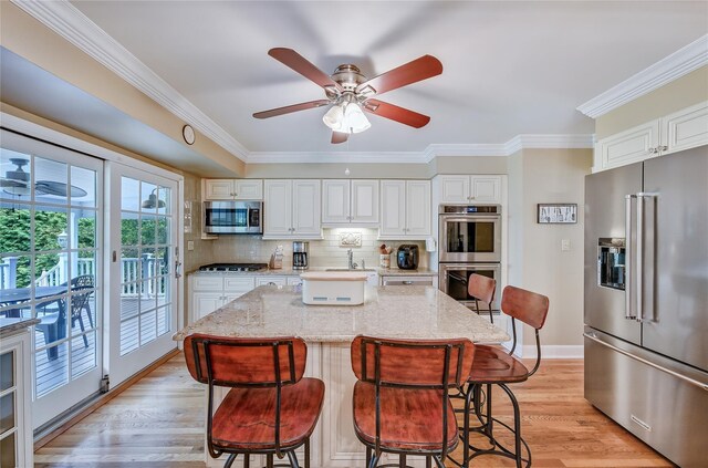 15 Eastover Dr, East Northport, NY 11731 - kitchen featuring stainless steel appliances, light stone counters, a kitchen breakfast bar, crown molding, and decorative backsplash