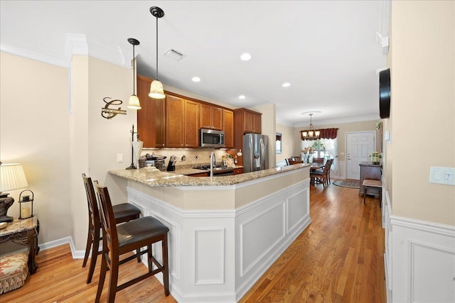 102 Paget Ln, Massapequa, NY 11758 - kitchen featuring appliances with stainless steel finishes, brown cabinets, a peninsula, light wood-style floors, and ornamental molding