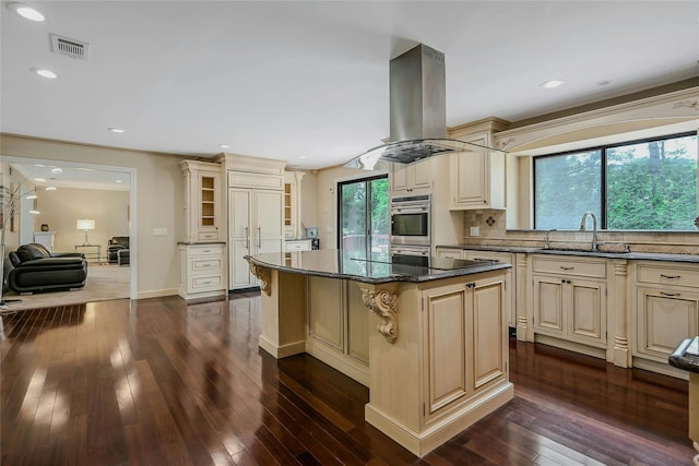 160 Coachman Pl E, Syosset, NY 11791 - kitchen featuring cream cabinetry, island exhaust hood, a kitchen island, dark wood-style flooring, and tasteful backsplash