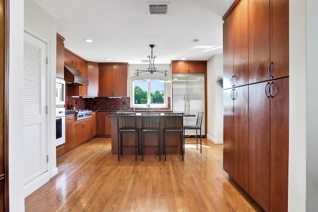 2 Harbor Ln Unit 301, New Rochelle, NY 10805 - kitchen with under cabinet range hood, appliances with stainless steel finishes, light wood-type flooring, decorative backsplash, and a breakfast bar