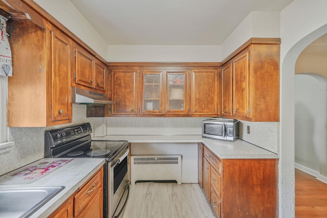 662 Rose Blvd, Baldwin, NY 11510 - kitchen with appliances with stainless steel finishes, radiator, under cabinet range hood, arched walkways, and light wood-type flooring