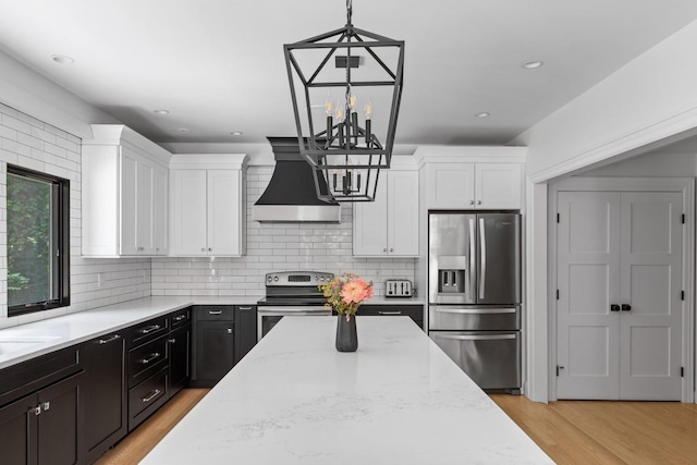9 Guthrie Ct, East Northport, NY 11731 - kitchen with appliances with stainless steel finishes, range hood, white cabinetry, light stone counters, and light wood-style flooring
