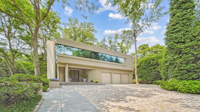 contemporary home featuring a garage, stucco siding, and decorative driveway