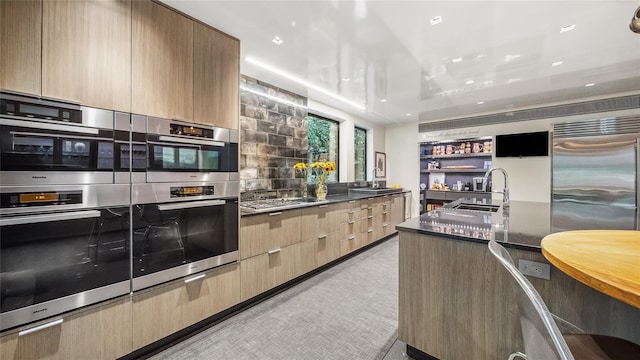 kitchen featuring modern cabinets, appliances with stainless steel finishes, dark countertops, light brown cabinets, and decorative backsplash