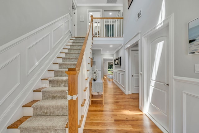 206 Brooksite Dr, Smithtown, NY 11787 - stairs with a decorative wall, crown molding, wood finished floors, a towering ceiling, and a wainscoted wall