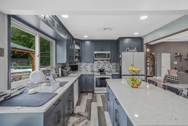 41 Linda St, Port Jefferson Station, NY 11776 - kitchen with appliances with stainless steel finishes, light stone counters, light wood-type flooring, tasteful backsplash, and glass insert cabinets