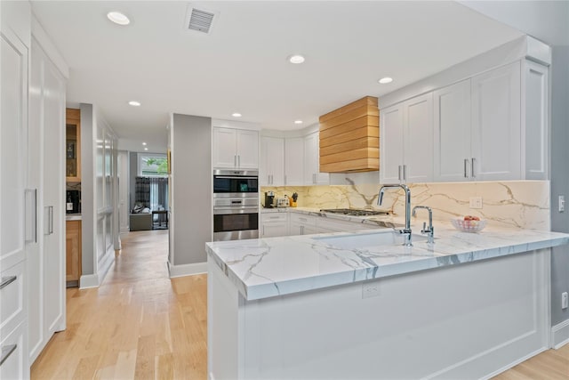 63 Sutton Pl, Manhasset, NY 11030 - kitchen featuring stainless steel double oven, light stone counters, custom range hood, light wood finished floors, and tasteful backsplash
