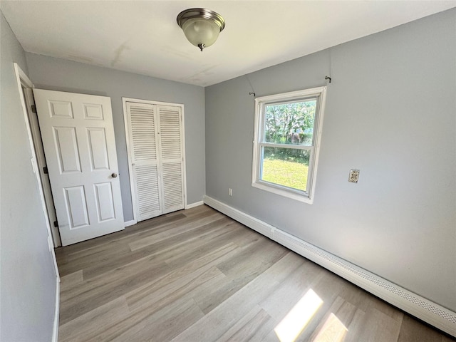 23 Chase Ln, Levittown, NY 11756 - unfurnished bedroom with a baseboard heating unit, light wood-style floors, and a closet