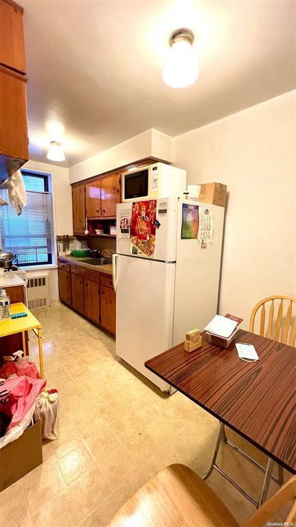 3815 149th St Unit 2D, Flushing, NY 11354 - kitchen with white appliances, brown cabinets, and radiator heating unit