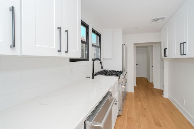 231 Macdougal St, Brooklyn, NY 11233 - kitchen featuring stainless steel appliances, white cabinets, light wood finished floors, light stone countertops, and decorative backsplash
