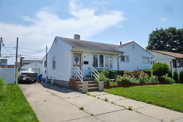 57 Hubbard Ave, Freeport, NY 11520 - view of front of house featuring a chimney, a front lawn, an outbuilding, a garage, and a shingled roof