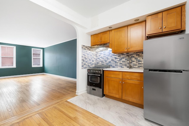 63109 Saunders St Unit 3A, Rego Park, NY 11374 - kitchen with appliances with stainless steel finishes, light countertops, under cabinet range hood, backsplash, and arched walkways