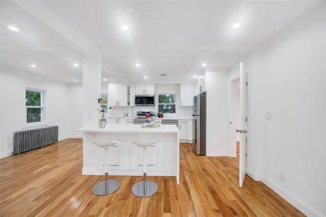 17 Pinetree Dr, Shirley, NY 11967 - kitchen featuring stainless steel appliances, radiator, light wood-style flooring, light countertops, and white cabinetry