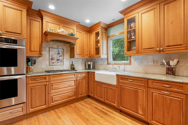 918 Sylvan Ln, Mamaroneck, NY 10543 - kitchen featuring stainless steel appliances, light wood-style floors, light stone counters, brown cabinetry, and backsplash