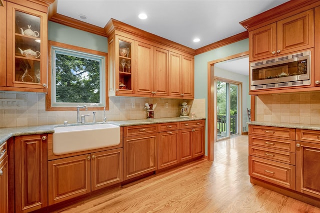 918 Sylvan Ln, Mamaroneck, NY 10543 - kitchen featuring stainless steel microwave, light wood finished floors, decorative backsplash, light stone countertops, and brown cabinetry