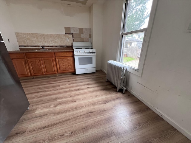 11617 141st St, Jamaica, NY 11436 - kitchen featuring white range with gas cooktop, radiator, brown cabinets, tasteful backsplash, and light wood-type flooring